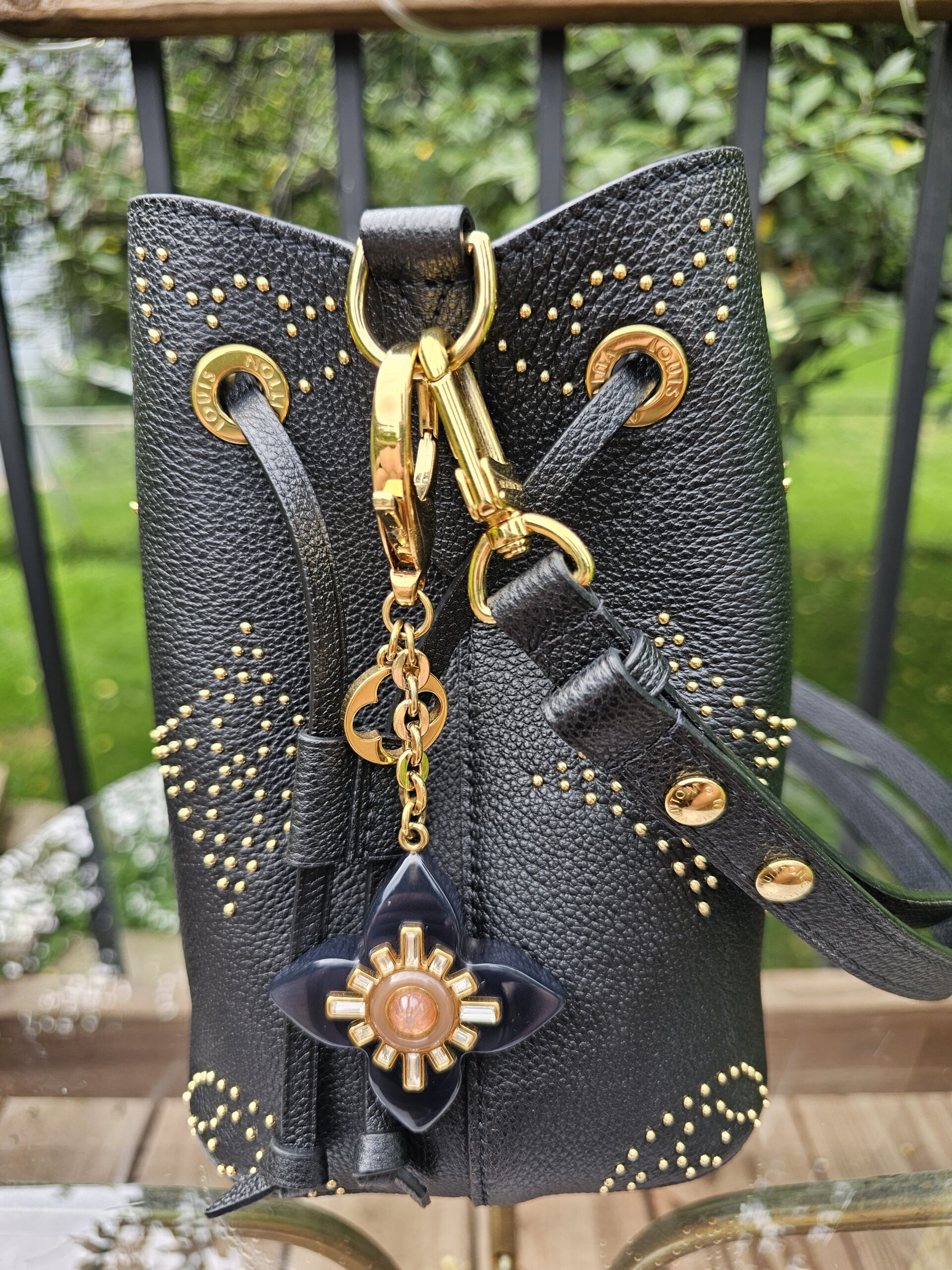 Louis Vuitton Fleur d Etoile charm hanging from a black studded handbag, shown for scale