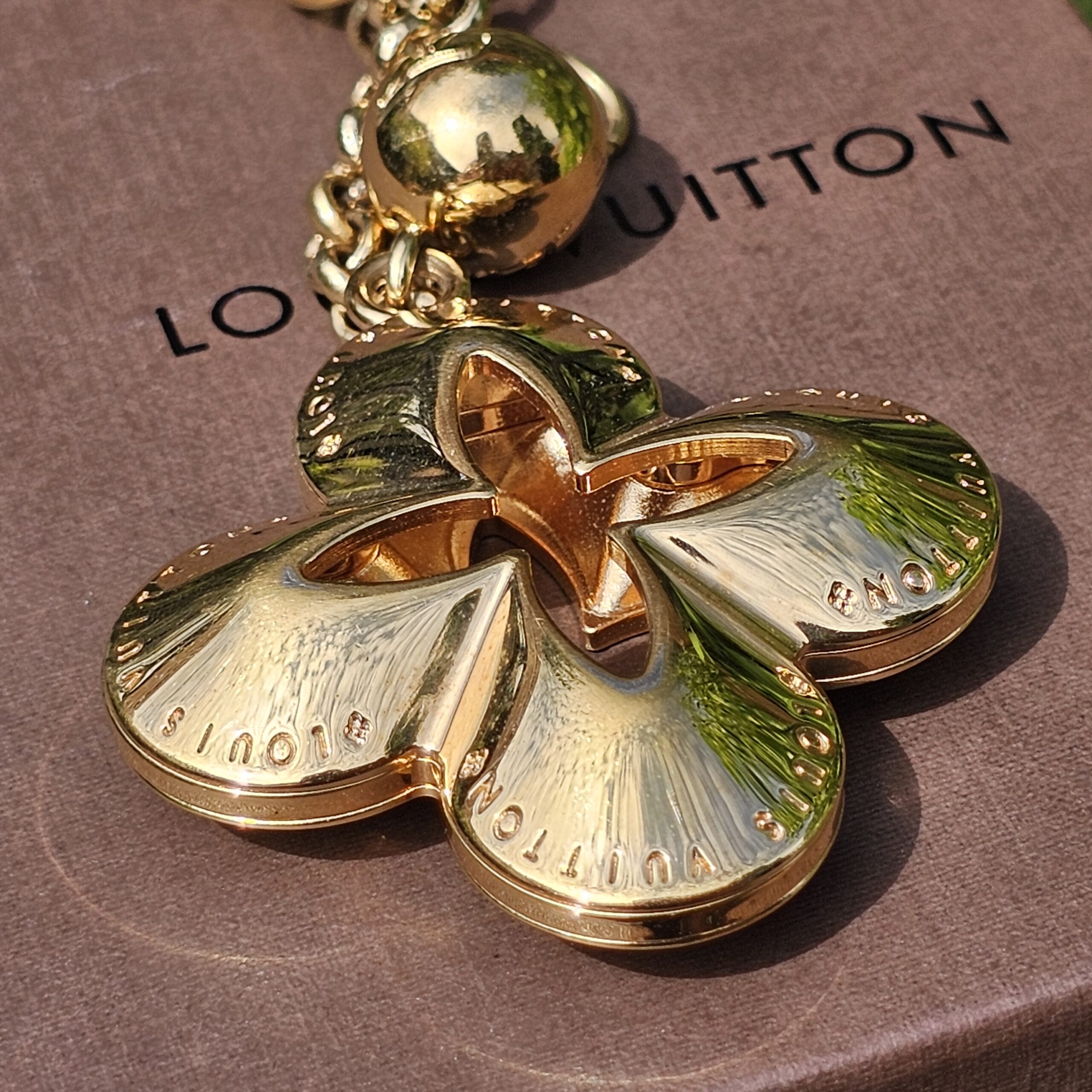 Close-up of the four-petal Monogram flower charm on the Louis Vuitton Eclipse gold-tone bag charm