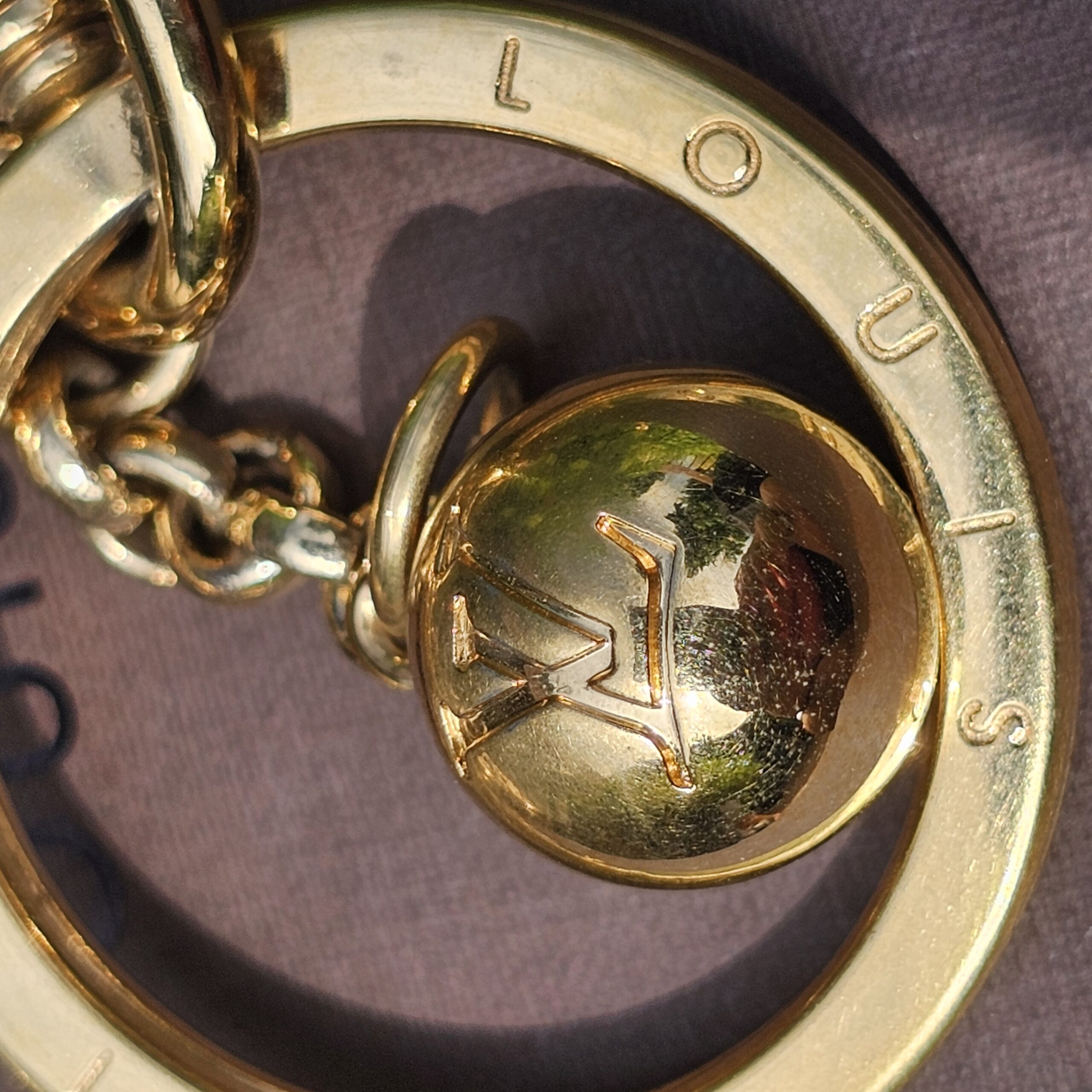 LV logo sphere charm inside the engraved Louis Vuitton ring on the Eclipse gold-tone key holder
