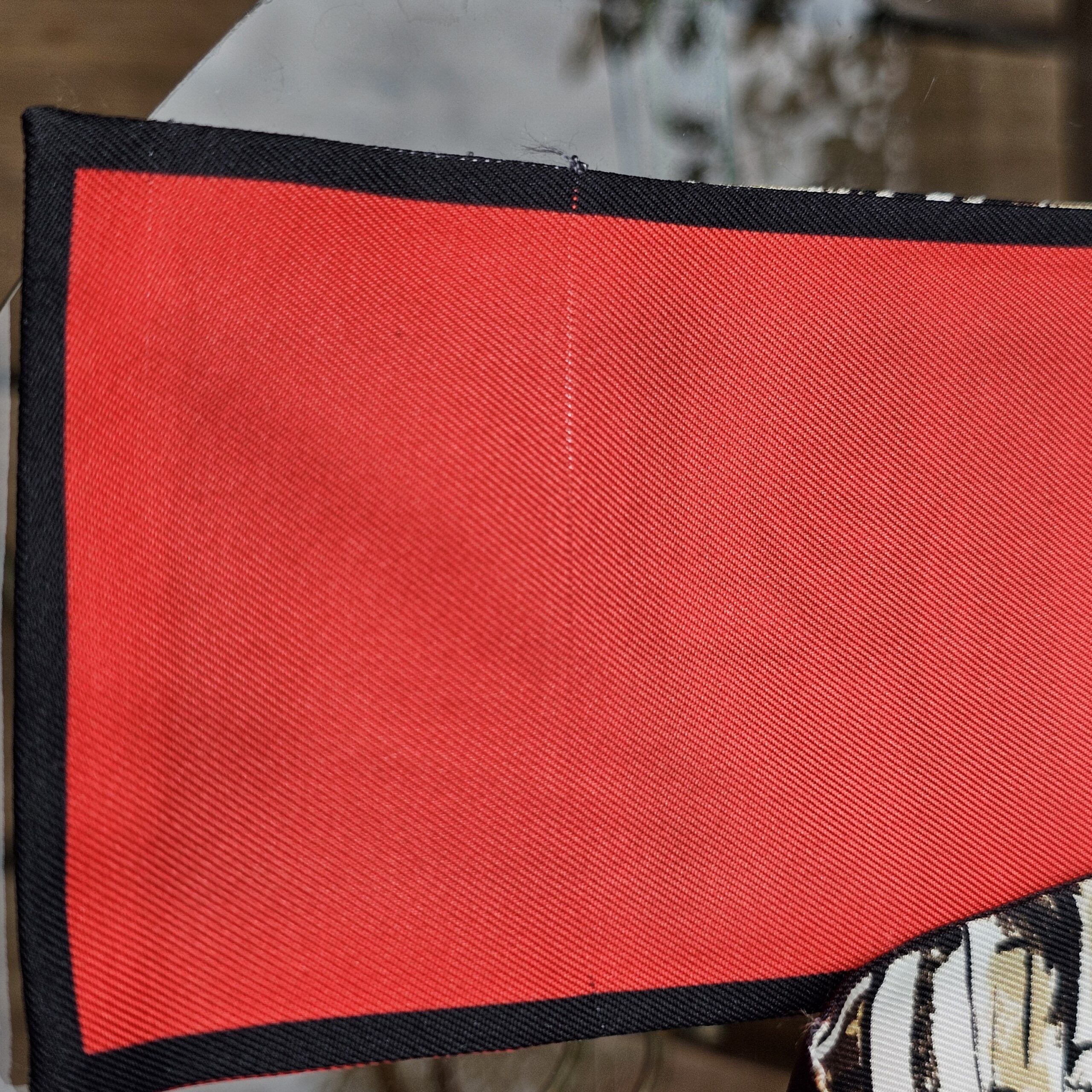 Red silk end panel of the Louis Vuitton Trunks bandeau with hand-rolled navy border