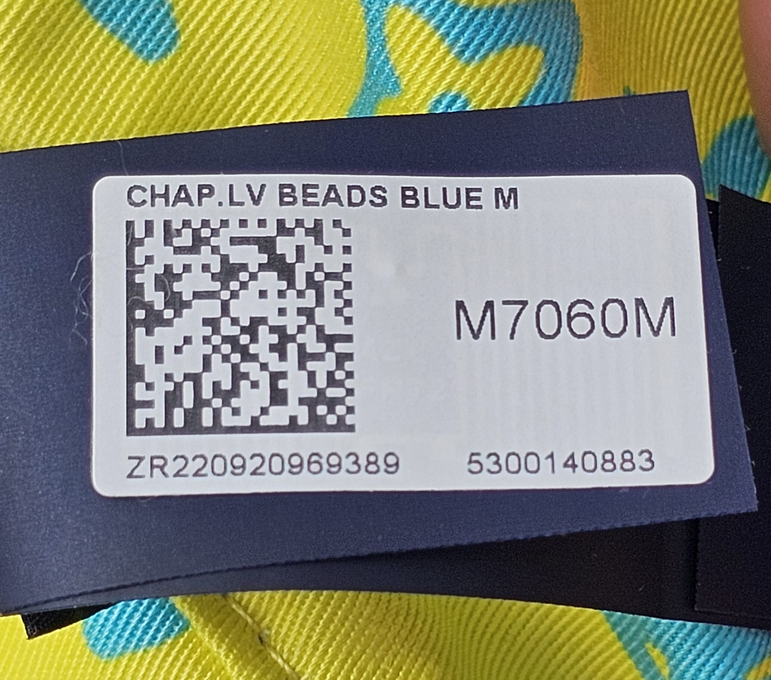 Retail tag for the Louis Vuitton Virgil Abloh bucket hat reading CHAP LV BEADS BLUE M with style number M7060M