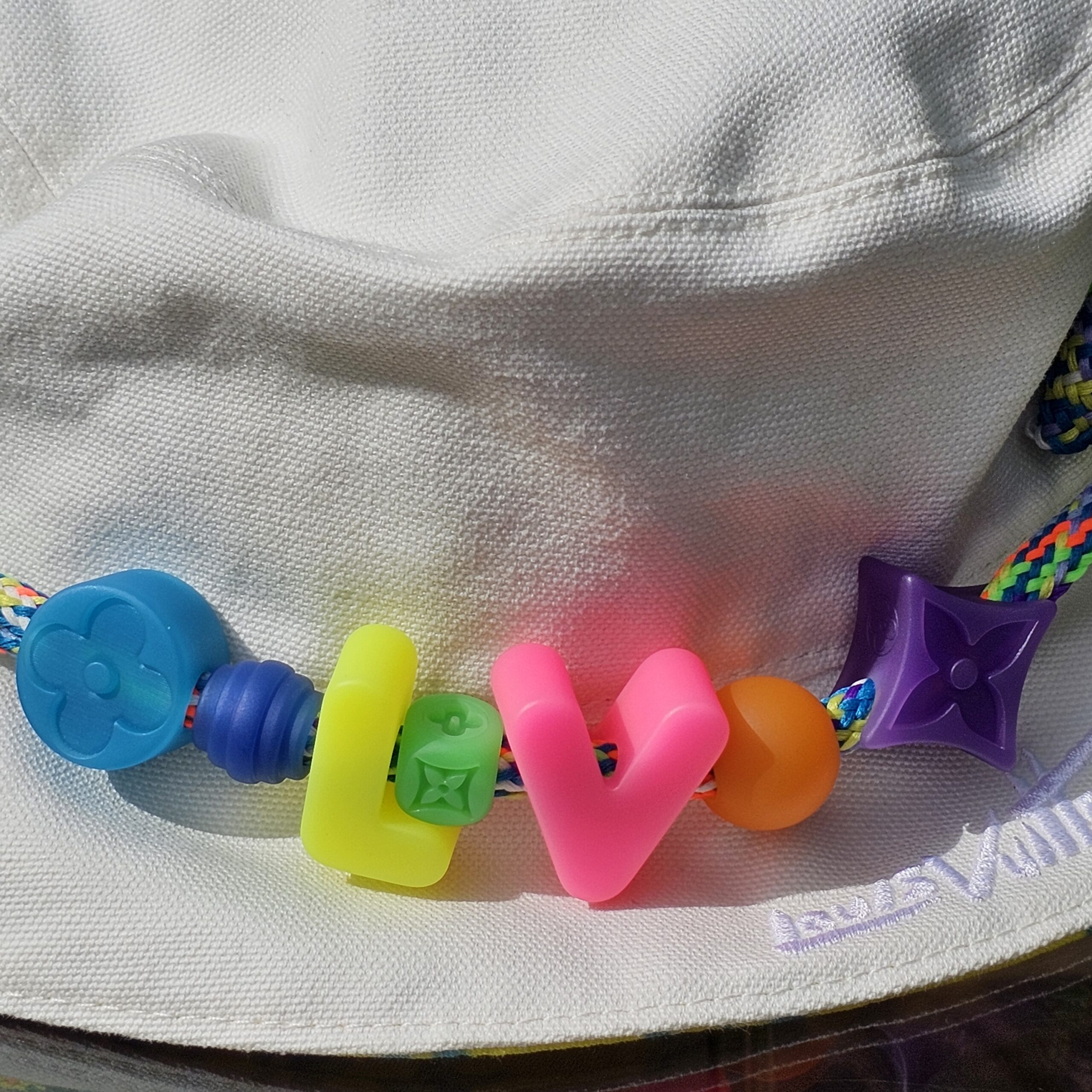 Close-up of the LV flower and letter beads on the cord of the Louis Vuitton Virgil Abloh bucket hat
