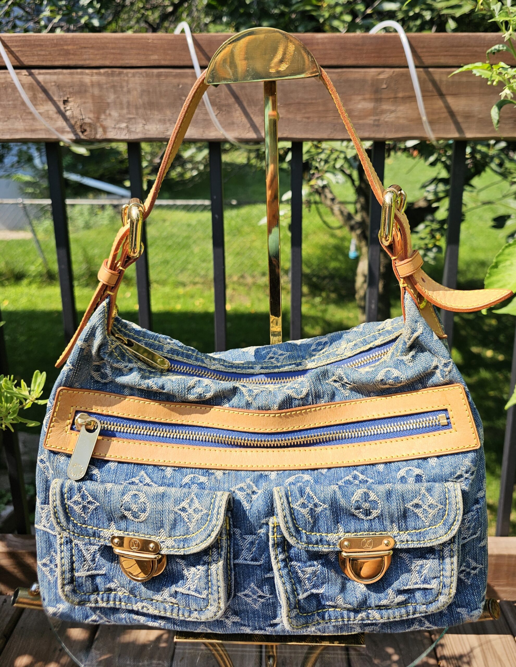 Front view of the Louis Vuitton Monogram Denim Baggy PM showing the exterior zip pocket and two flap pockets with gold-tone hardware