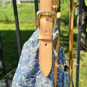 Natural vachetta leather shoulder strap and gold-tone buckle on the Louis Vuitton Monogram Denim Baggy PM