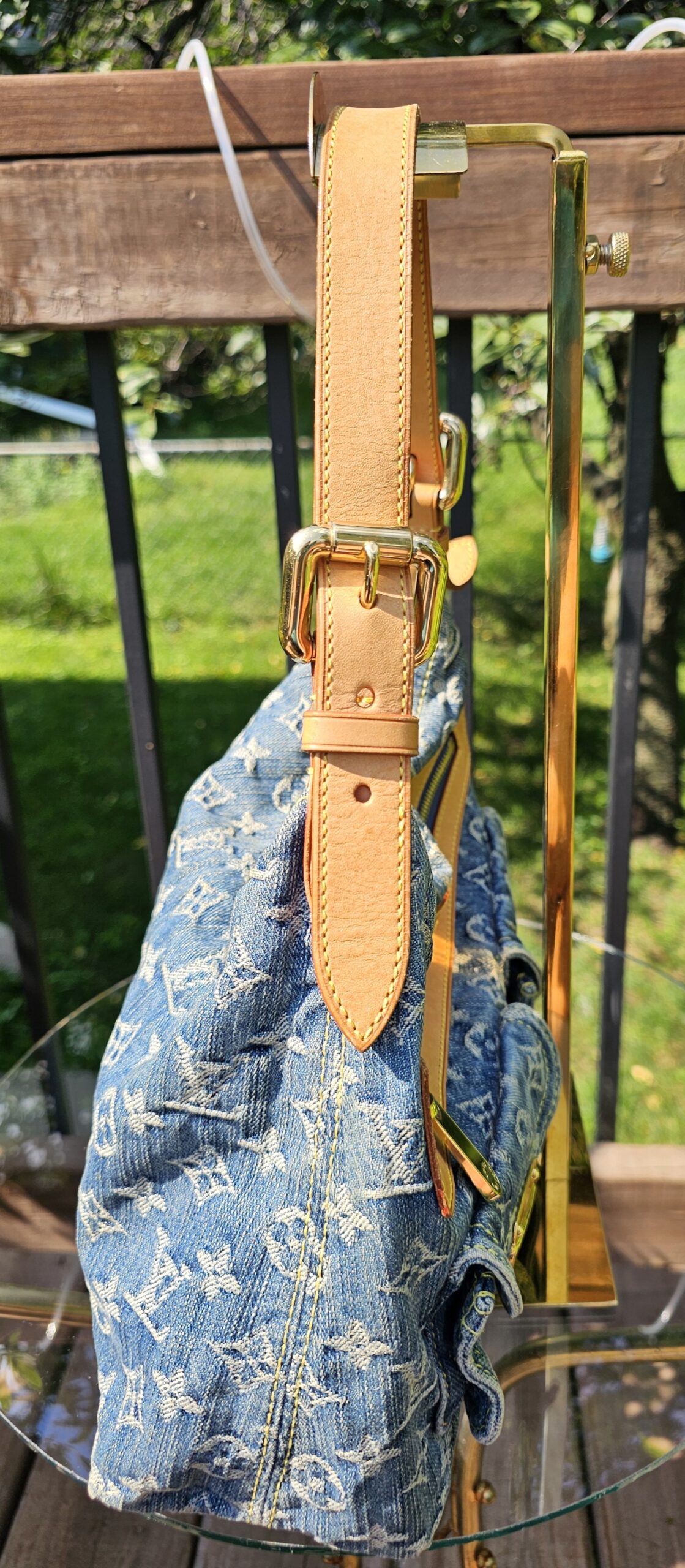 Natural vachetta leather shoulder strap and gold-tone buckle on the Louis Vuitton Monogram Denim Baggy PM