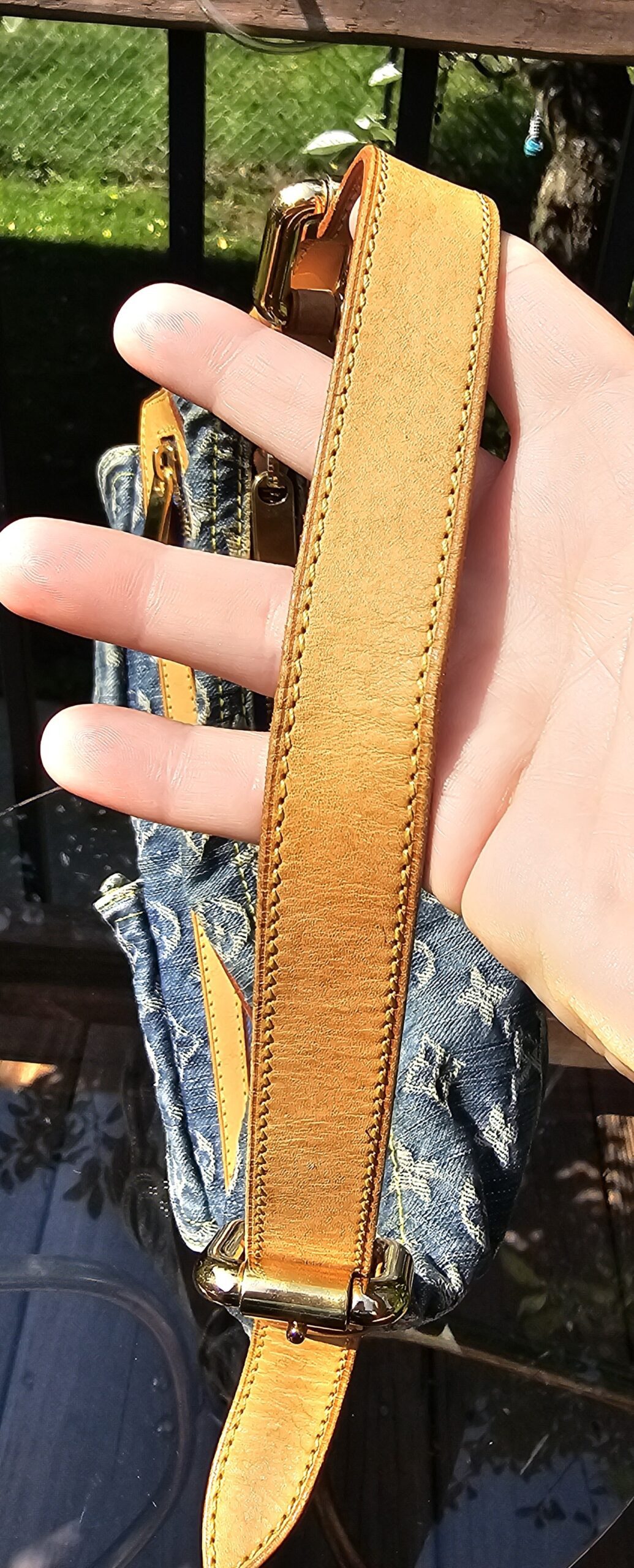 Vachetta strap of the Louis Vuitton Monogram Denim Baggy PM held in hand showing warm patina and light wear