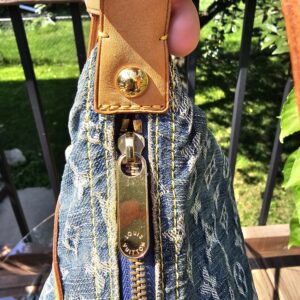 Vachetta leather tab and gold-tone hardware attaching the strap to the Louis Vuitton Monogram Denim Baggy PM