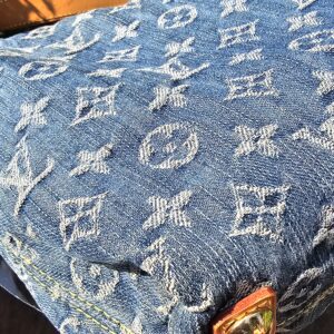 Corner of the Louis Vuitton Monogram Denim Baggy PM showing the vachetta tab and gold-tone stud