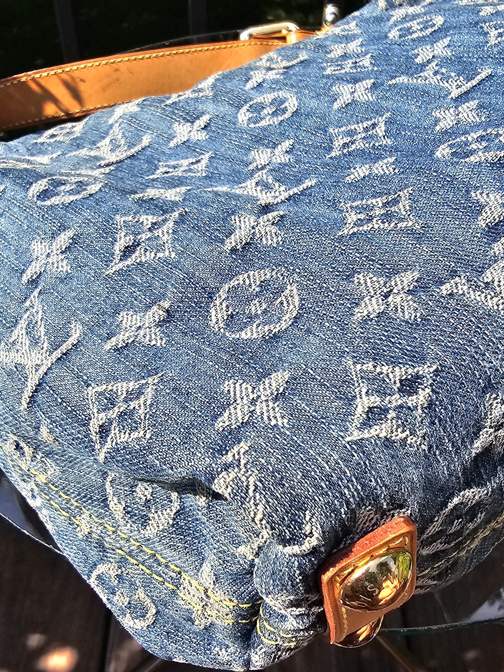 Corner of the Louis Vuitton Monogram Denim Baggy PM showing the vachetta tab and gold-tone stud