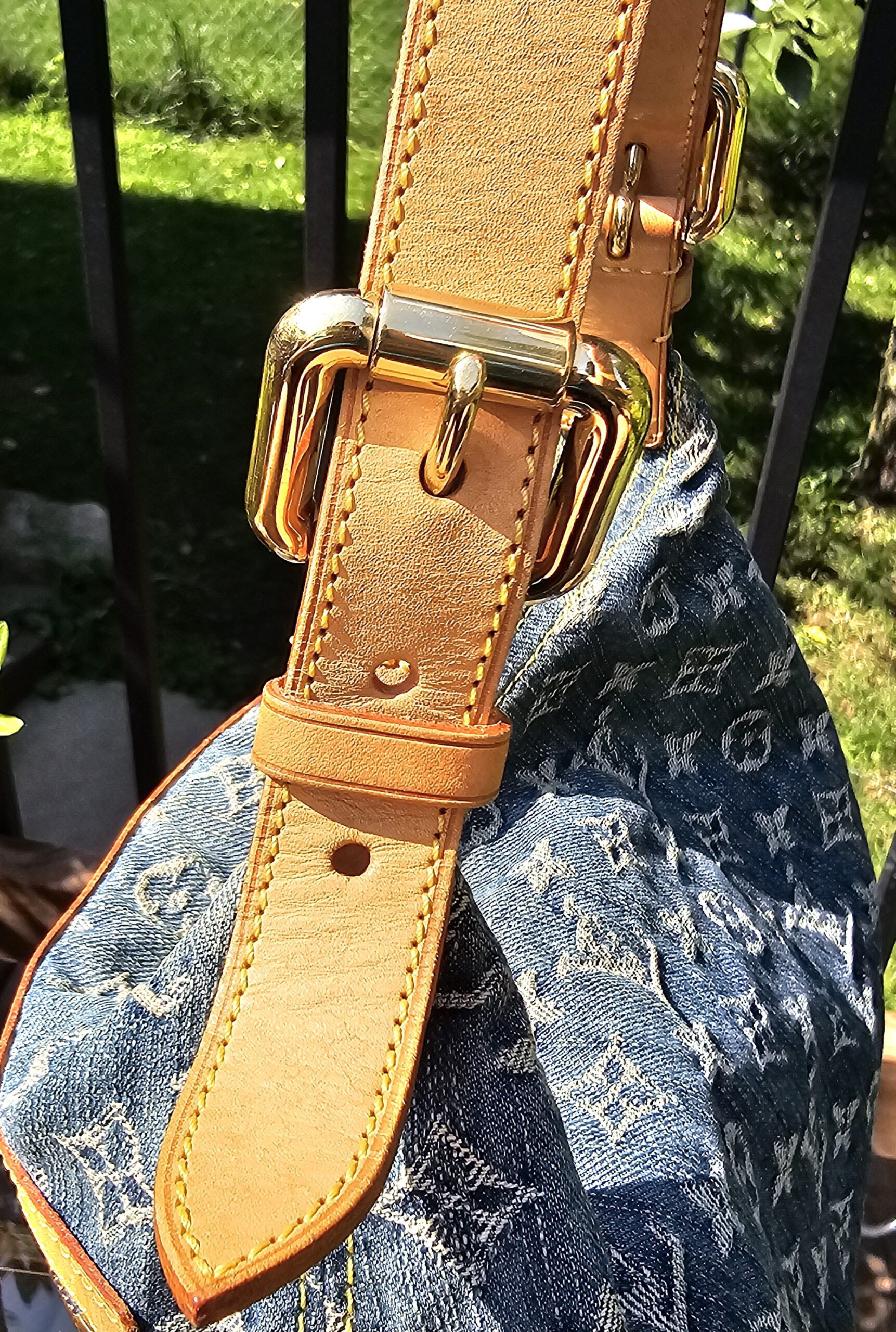 Close-up of the gold-tone strap buckle and vachetta punch holes on the Louis Vuitton Monogram Denim Baggy PM