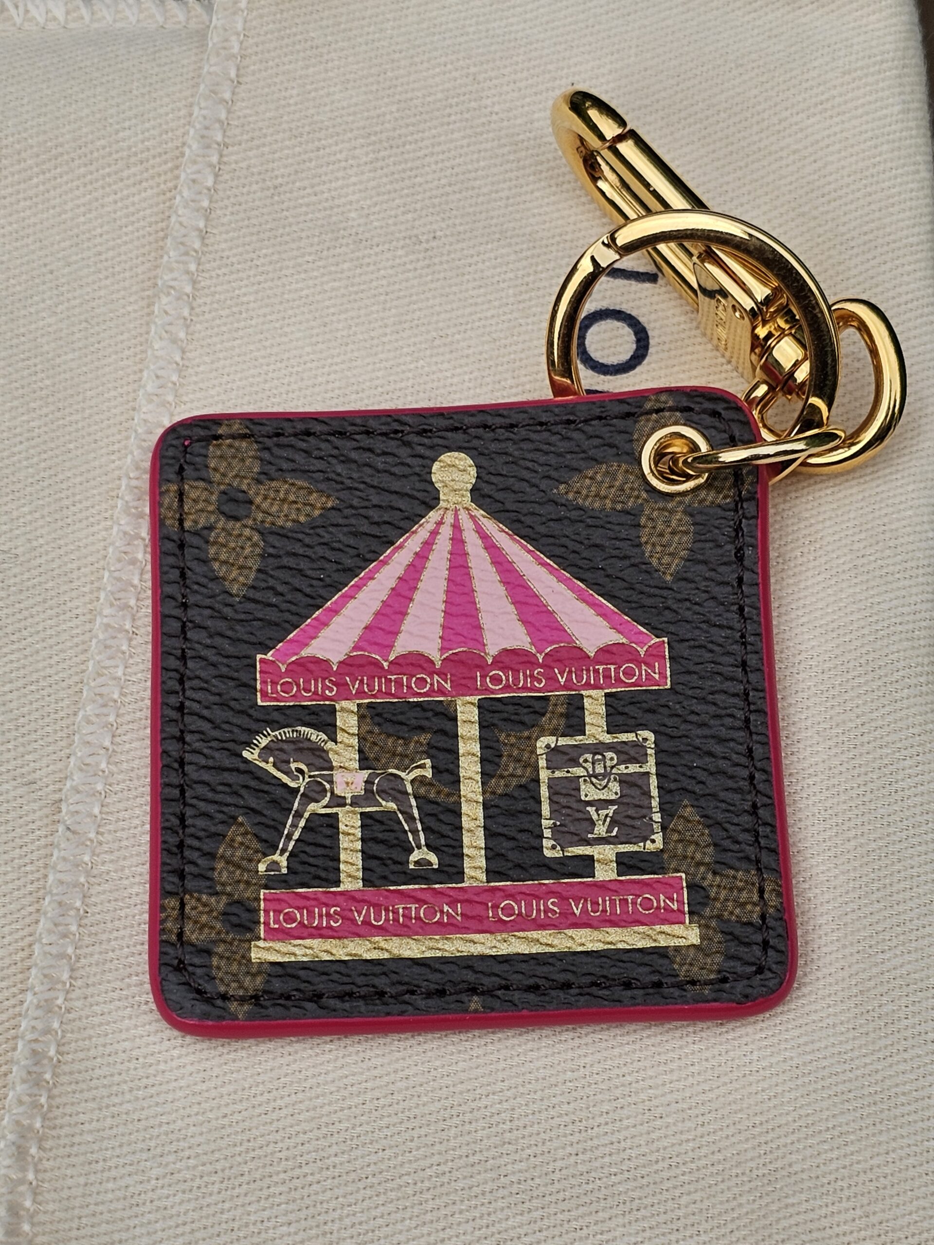 Pink carousel illustration with metallic gold accents on the Monogram canvas face of the Louis Vuitton Illustre charm