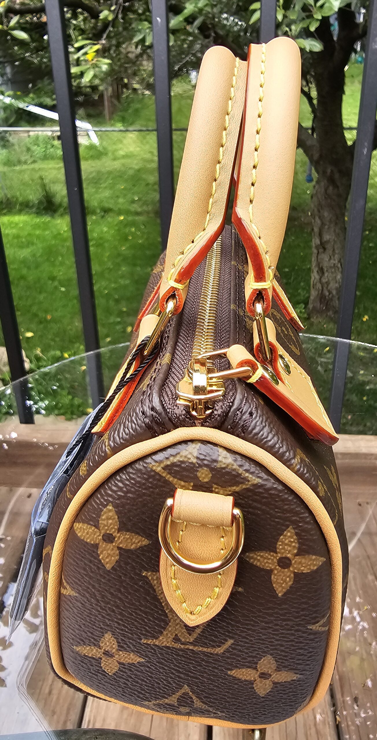 Side of the Louis Vuitton Nano Speedy Bandouliere showing the vachetta leather tab and gold-tone D-ring for the strap