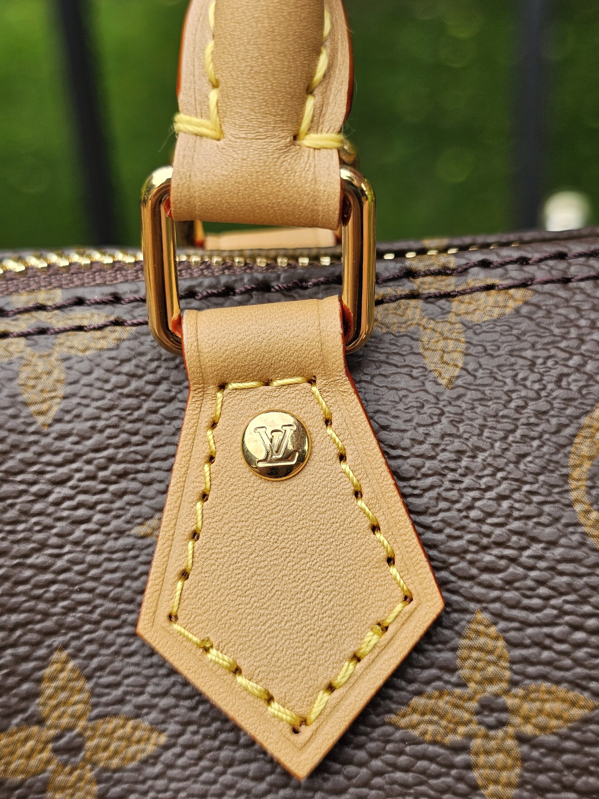 Close-up of the vachetta leather tab and gold-tone ring hardware on the side of the Louis Vuitton Nano Speedy Bandouliere