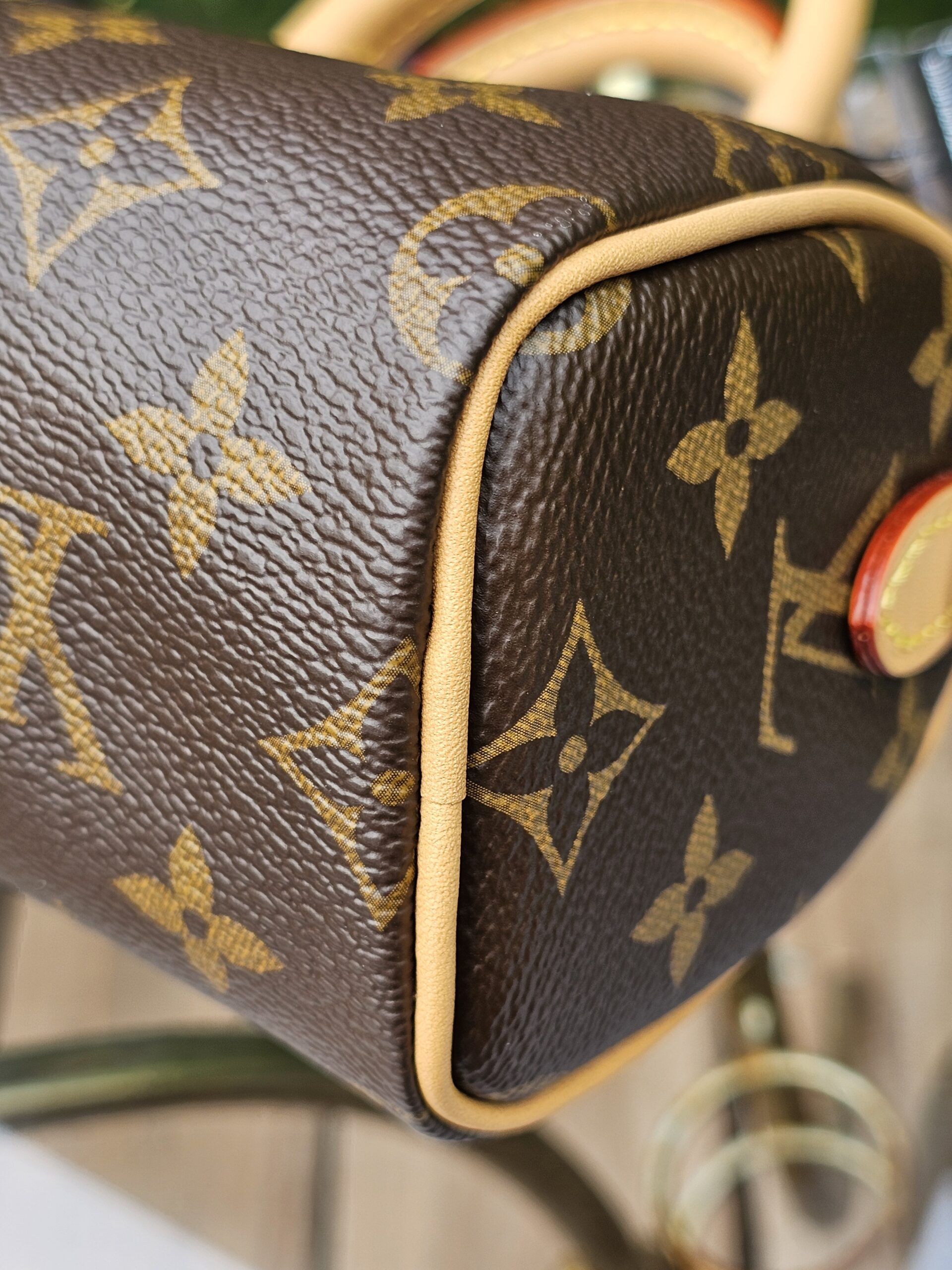 Corner of the Louis Vuitton Nano Speedy Bandouliere showing light vachetta piping over Monogram canvas