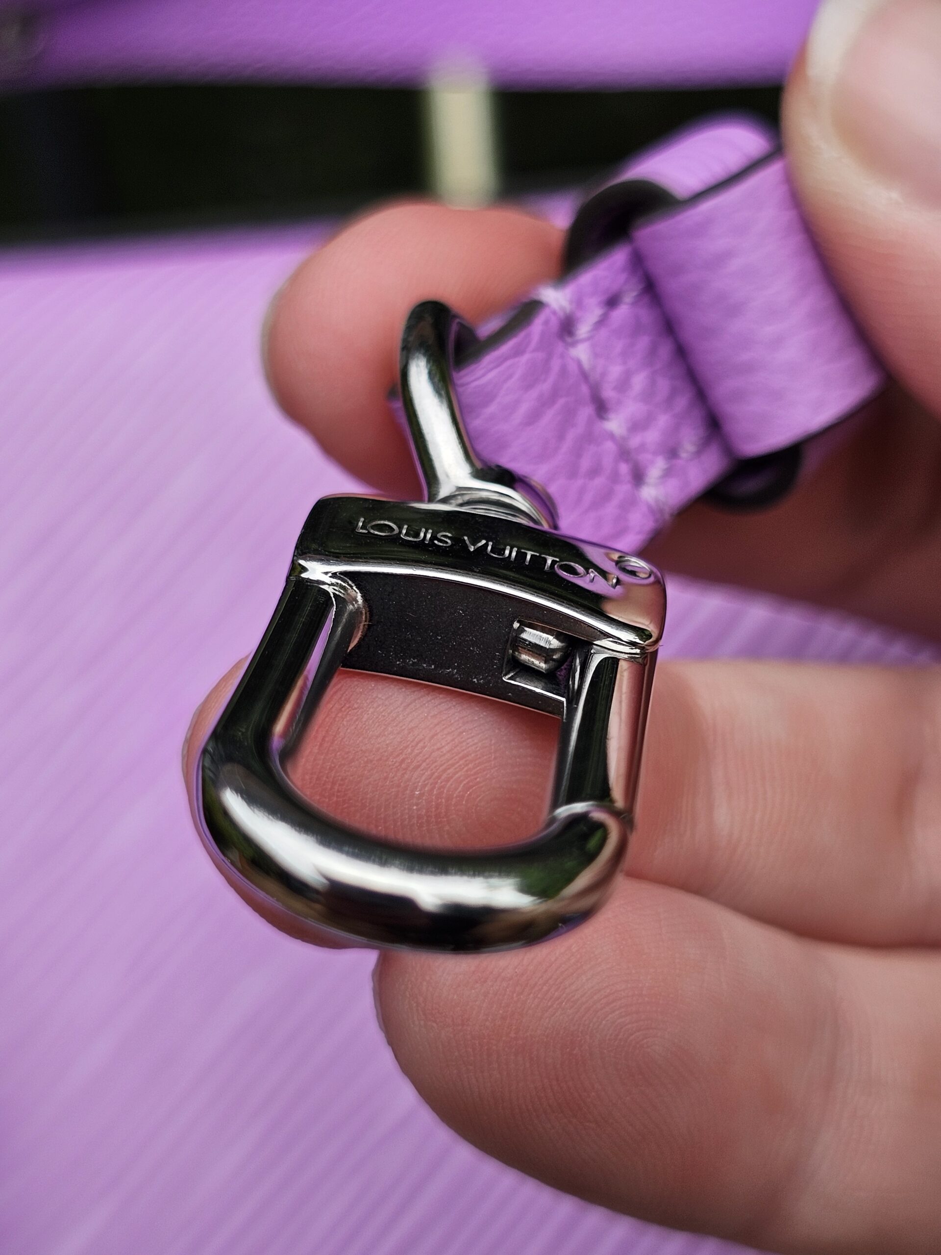 Single silver-tone clasp from the Louis Vuitton Epi Marellini strap held in hand