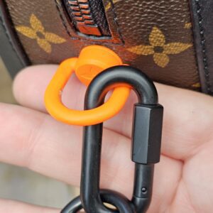 Orange and black Solar Ray carabiner clip on the Louis Vuitton Soft Trunk strap