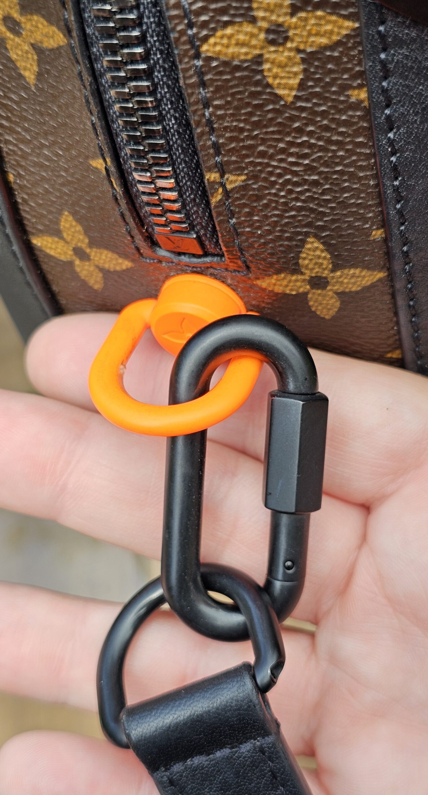 Orange and black Solar Ray carabiner clip on the Louis Vuitton Soft Trunk strap