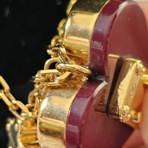 Gold-tone key charm hanging beside the burgundy heart on the Louis Vuitton Lock Me necklace