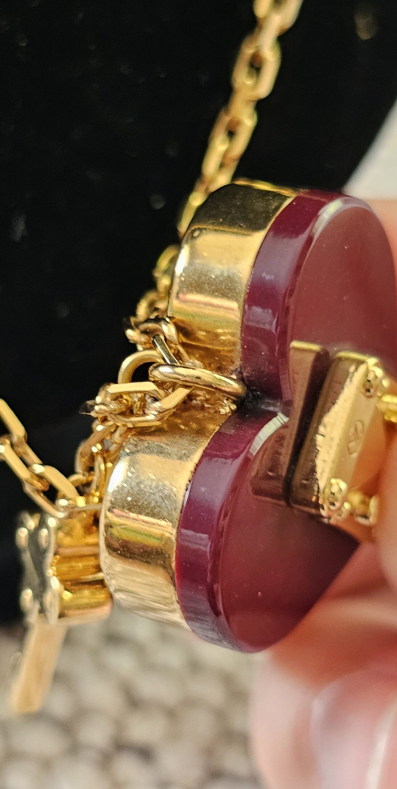 Gold-tone key charm hanging beside the burgundy heart on the Louis Vuitton Lock Me necklace