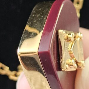 Louis Vuitton Lock Me heart pendant held in hand showing the burgundy resin and gold back