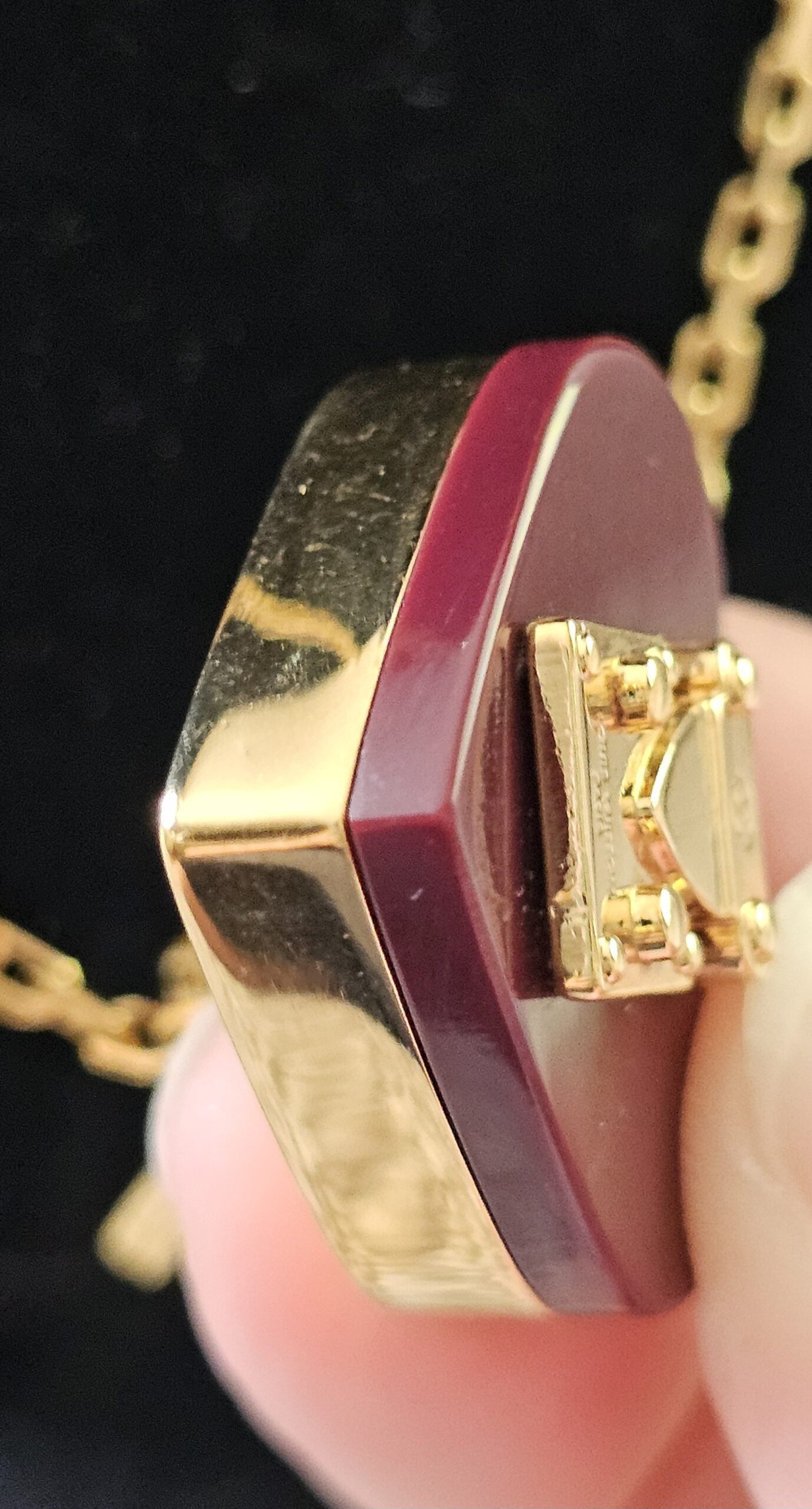Louis Vuitton Lock Me heart pendant held in hand showing the burgundy resin and gold back