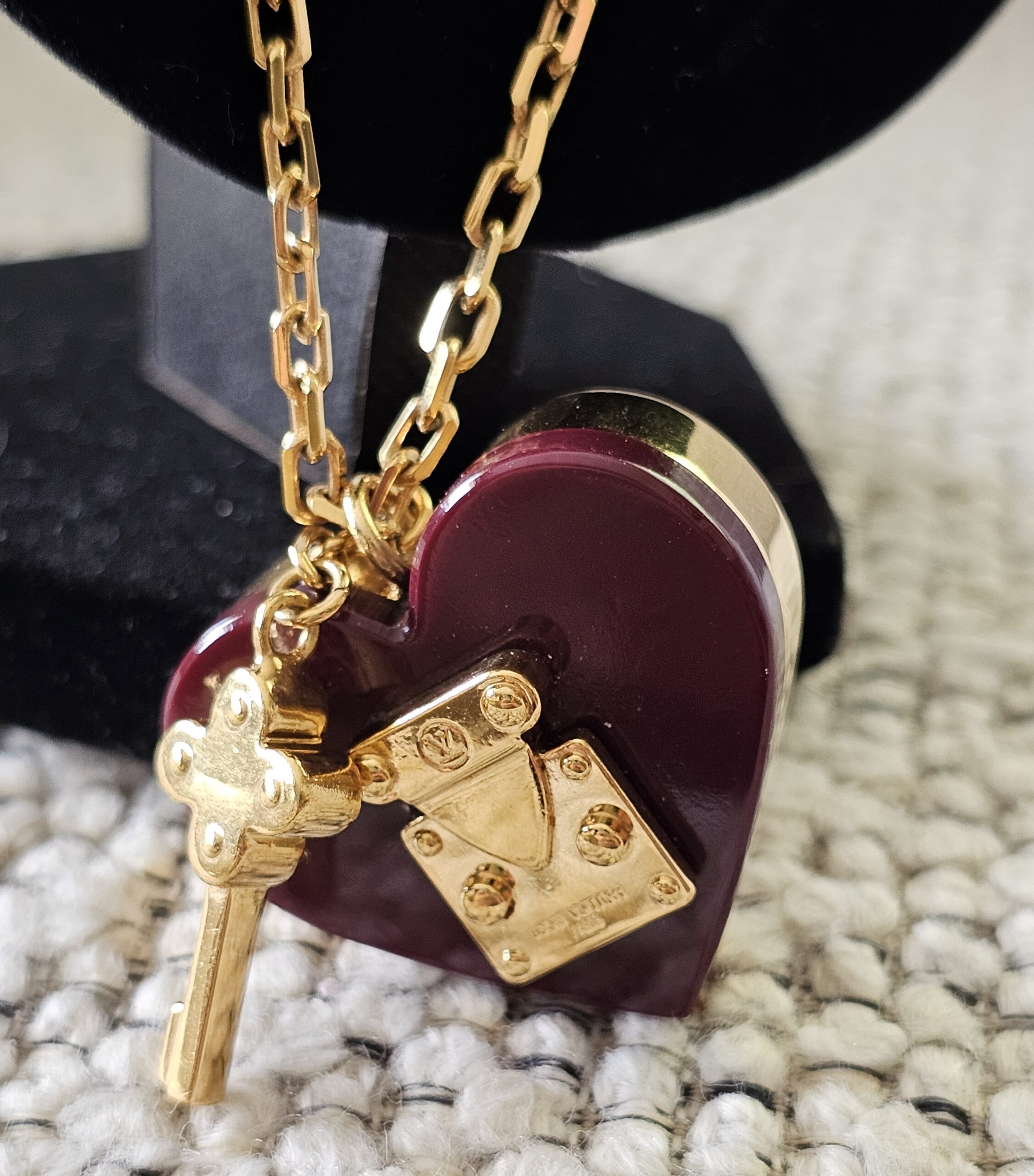 Burgundy heart pendant and gold key charm of the Louis Vuitton Lock Me necklace shown together