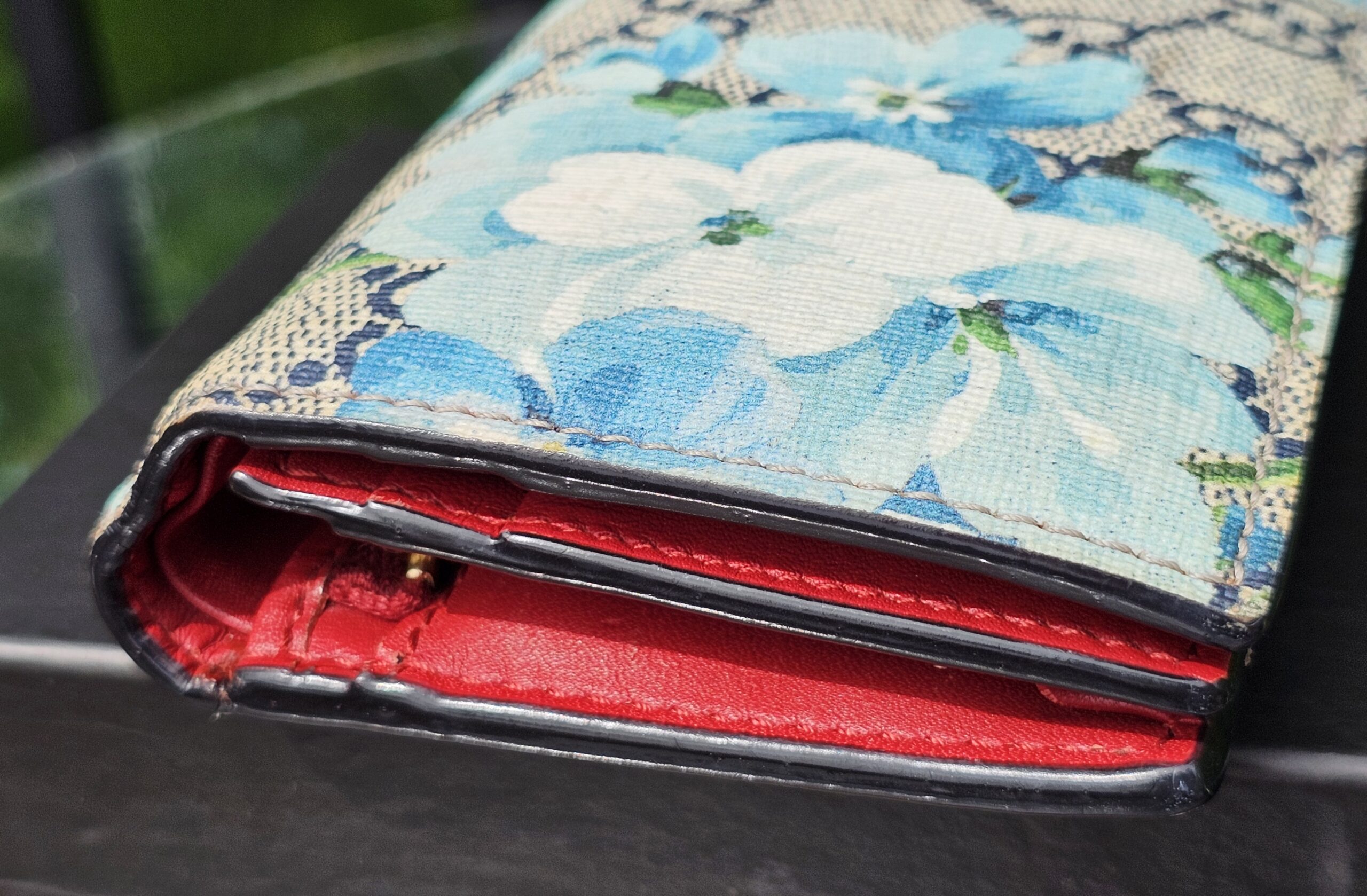 Gucci Blooms compact wallet showing the vibrant red leather interior against the blue floral canvas
