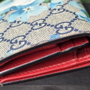 Angled view of the Gucci GG Supreme Blooms compact wallet with red interior visible