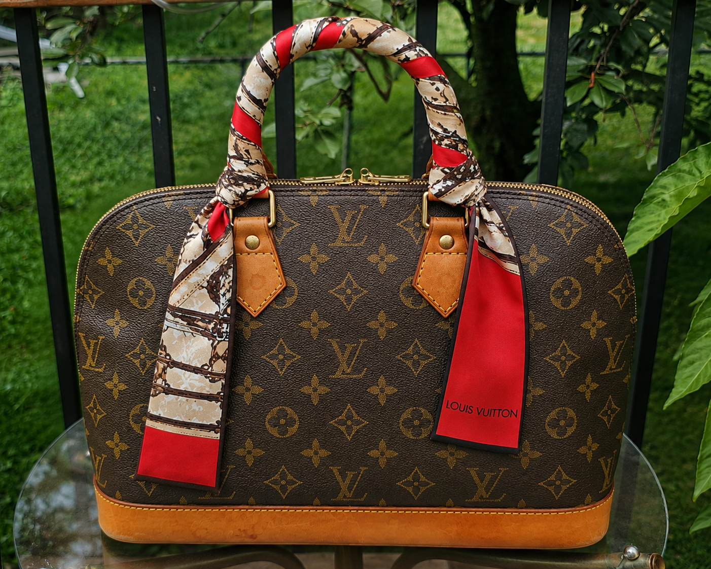 Louis Vuitton silk Trunks bandeau tied around the handle of a Monogram handbag