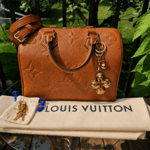 Louis Vuitton Eclipse gold-tone key holder and bag charm hanging from a leather handbag, shown for scale