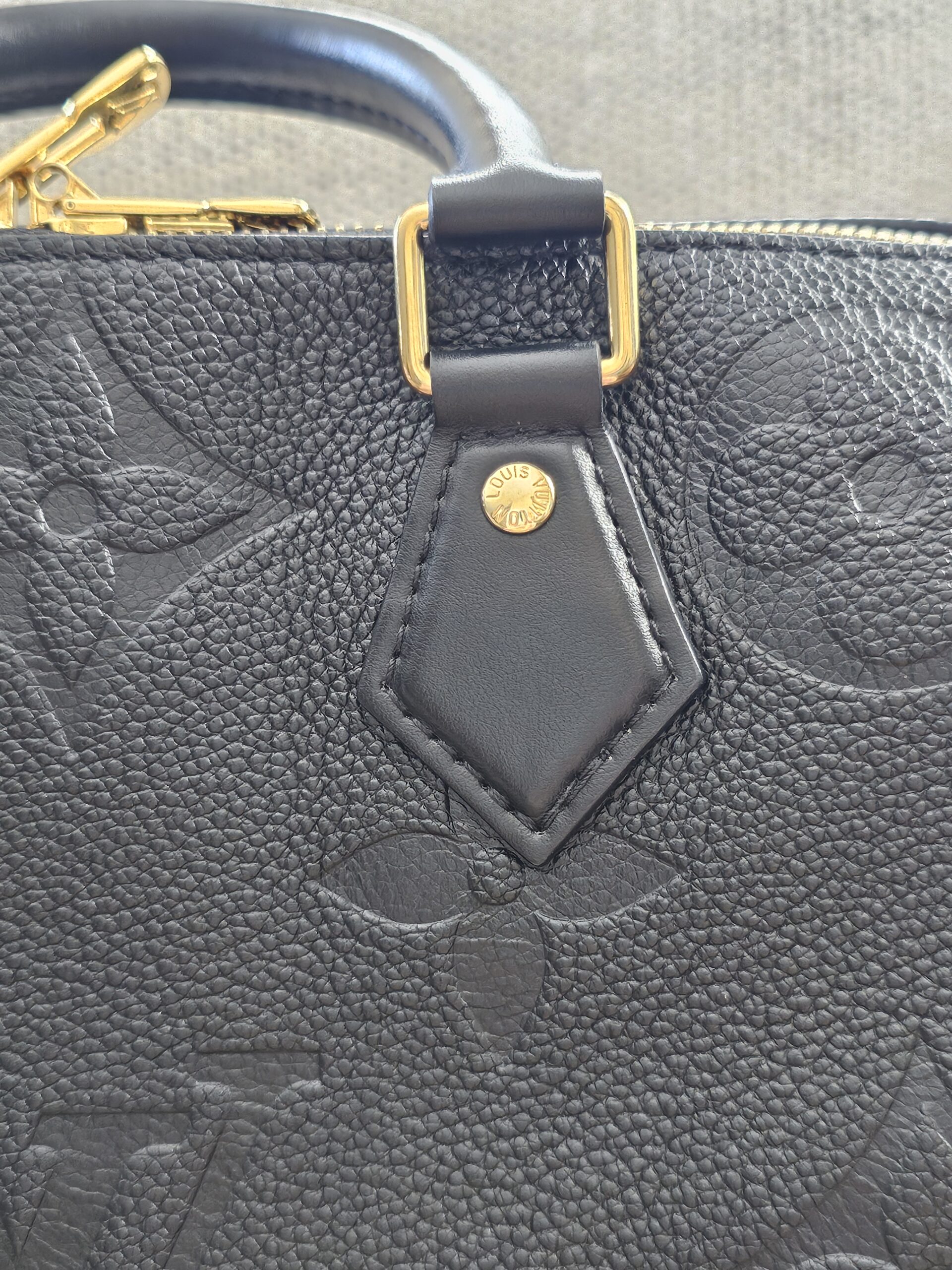 Leather tab and gold-tone stud on the black Giant Monogram Empreinte Speedy Bandouliere 25
