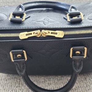 Gold-tone zipper pulls and engraved LV padlock on the black Empreinte Speedy Bandouliere 25