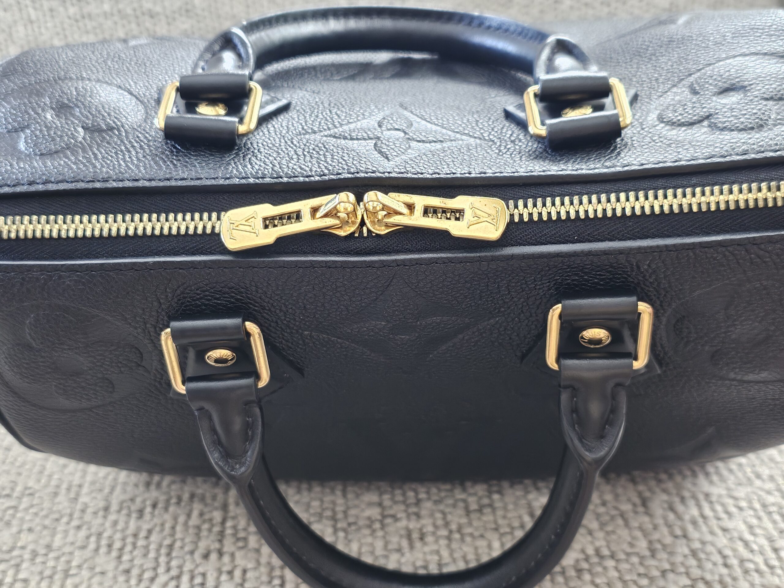 Gold-tone zipper pulls and engraved LV padlock on the black Empreinte Speedy Bandouliere 25
