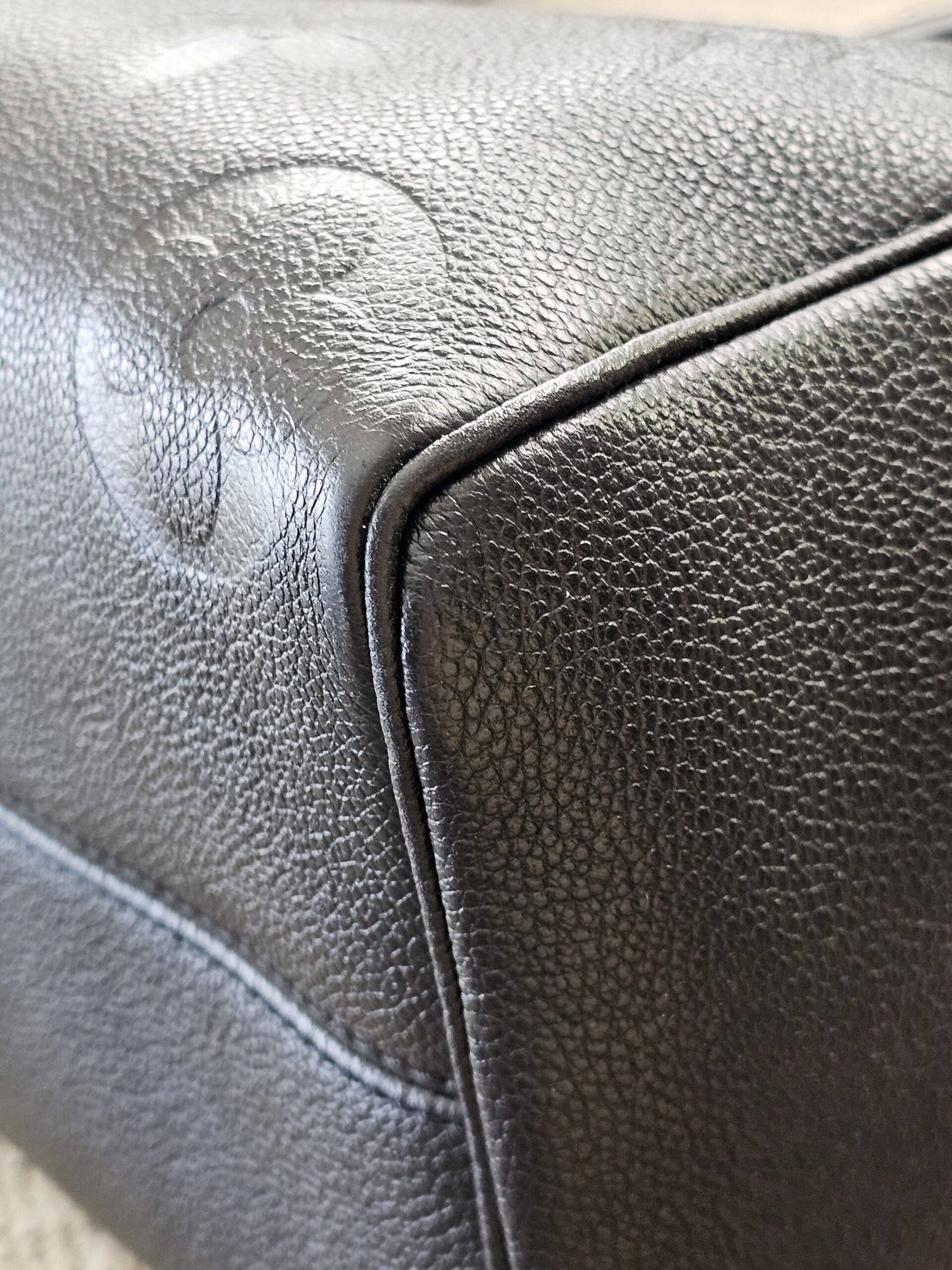 Bottom corner of the black Empreinte Speedy Bandouliere 25 with embossed monogram detail