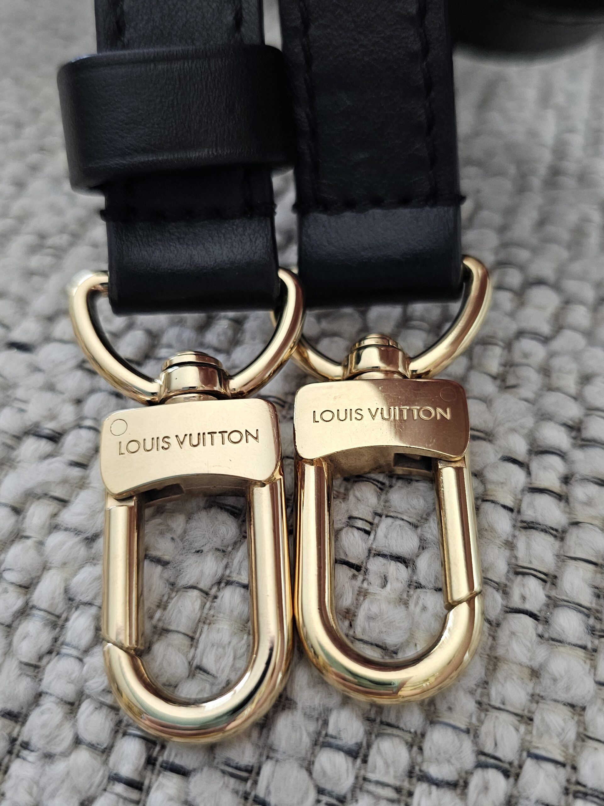 Engraved gold-tone snap hooks on the black leather shoulder strap of the Speedy Bandouliere 25
