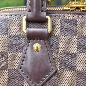 Gold-tone D-ring and leather handle tab on the Damier Ebene Speedy Bandouliere 20