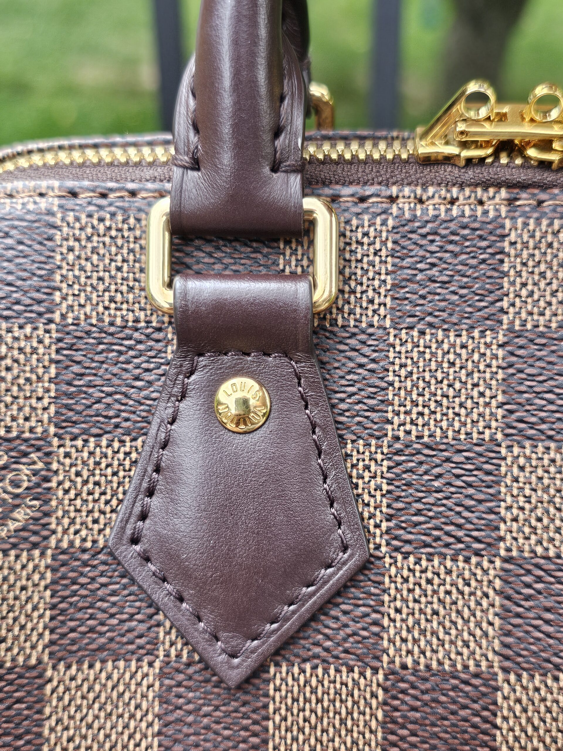 Gold-tone D-ring and leather handle tab on the Damier Ebene Speedy Bandouliere 20