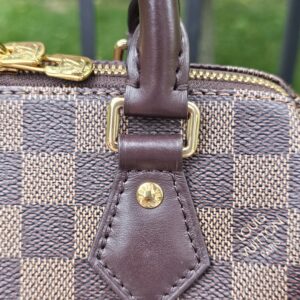 Leather handle tab beside the zipper end on the Damier Ebene Speedy Bandouliere 20