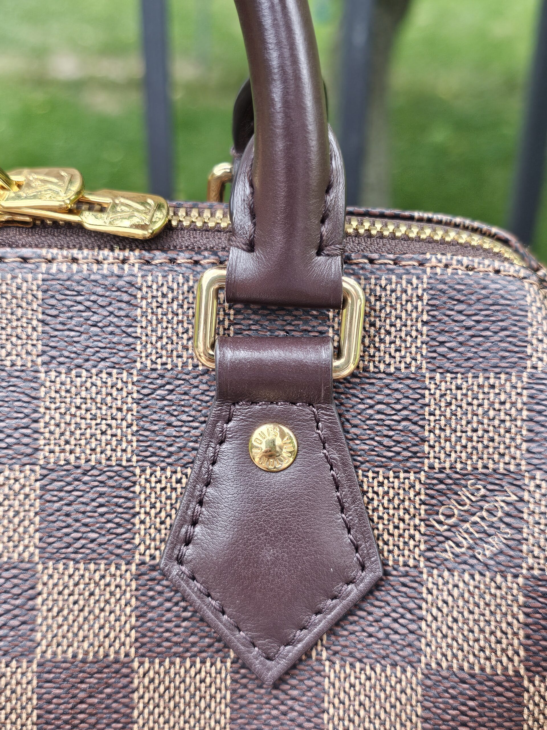 Leather handle tab beside the zipper end on the Damier Ebene Speedy Bandouliere 20