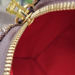 Gold-tone zipper against the red lining of the Damier Ebene Speedy Bandouliere 20