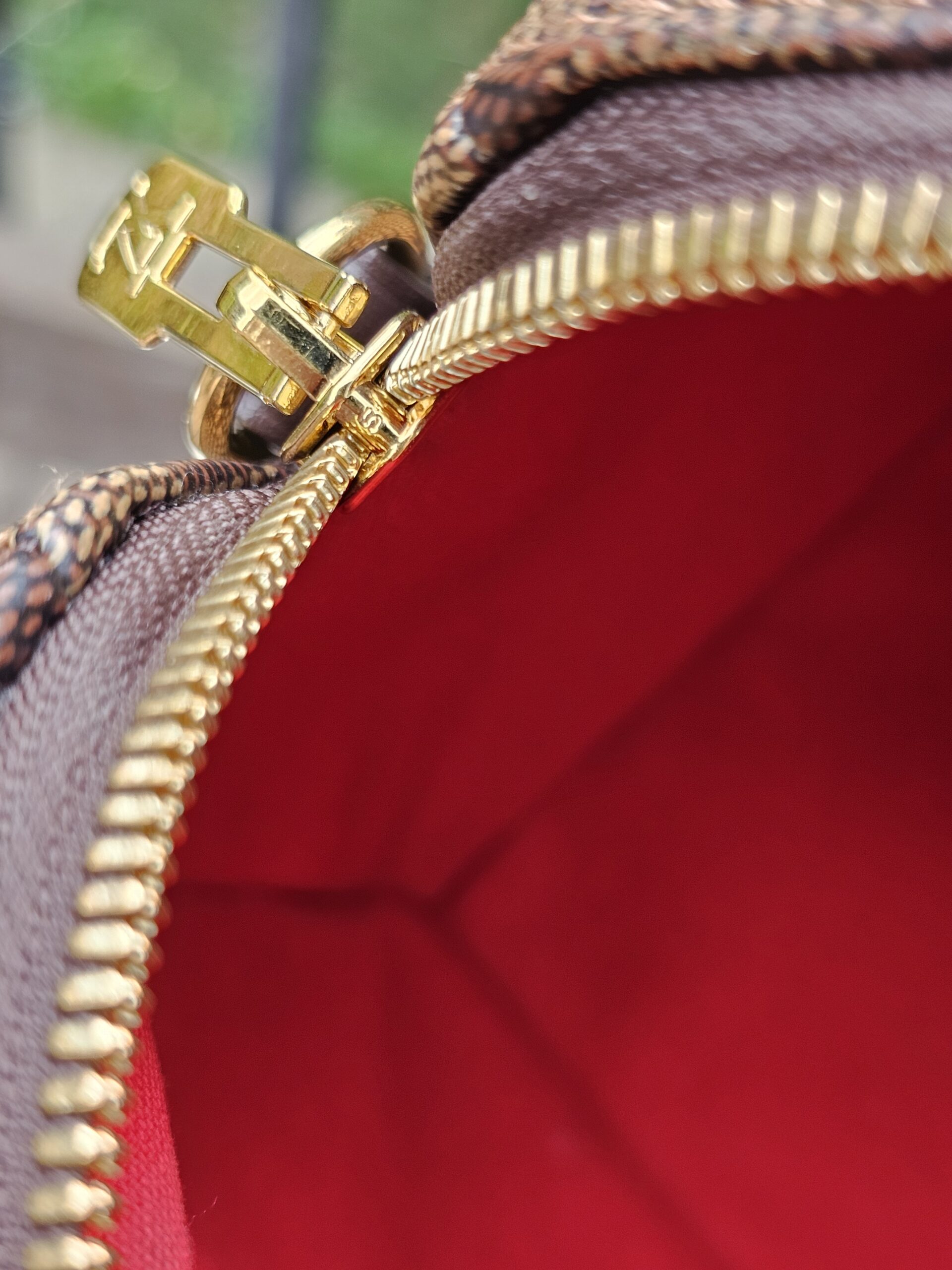 Gold-tone zipper against the red lining of the Damier Ebene Speedy Bandouliere 20