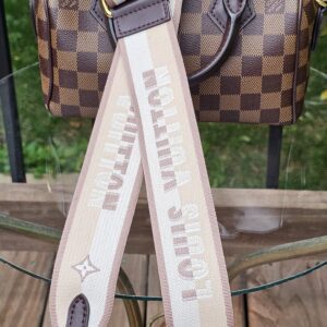 Damier Ebene Speedy Bandouliere 20 laid out with its beige monogram jacquard shoulder strap