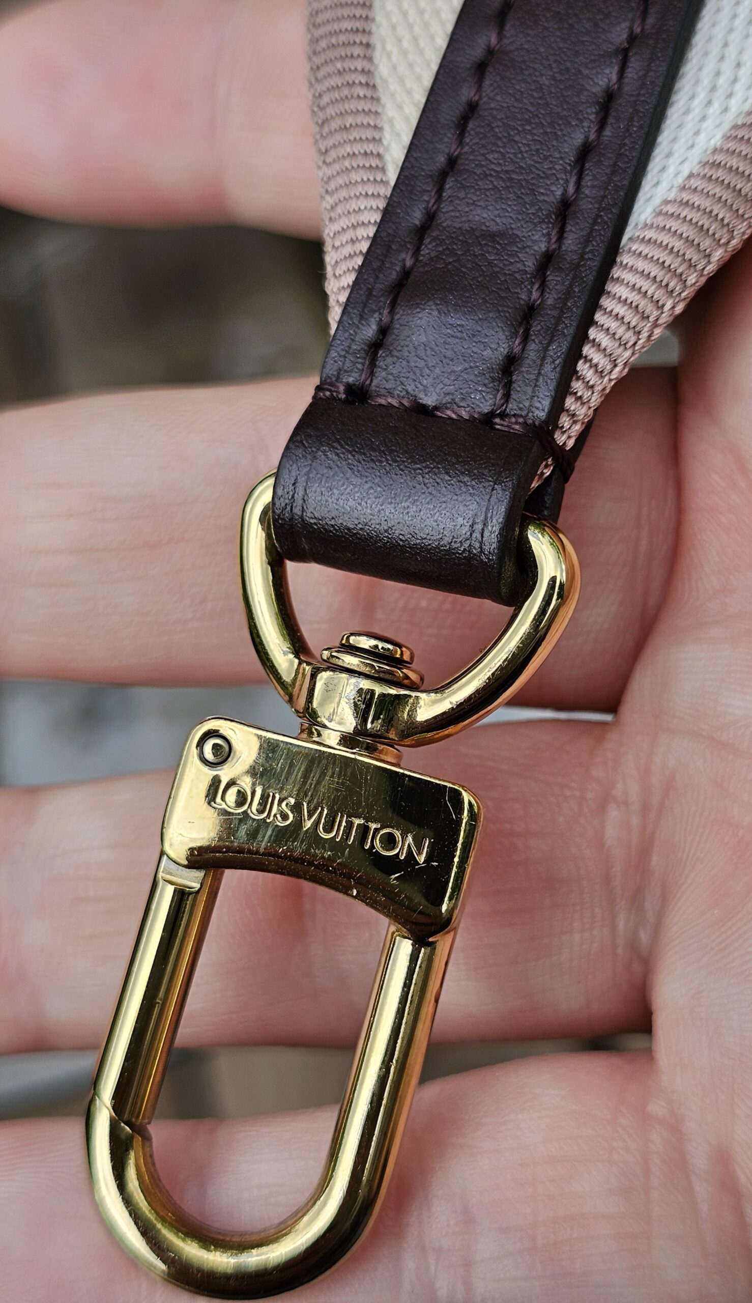 Close-up of an engraved gold-tone snap hook on the Louis Vuitton jacquard shoulder strap