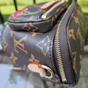 Side of the Cerises Mini Bumbag showing the curved zip and vachetta leather tab