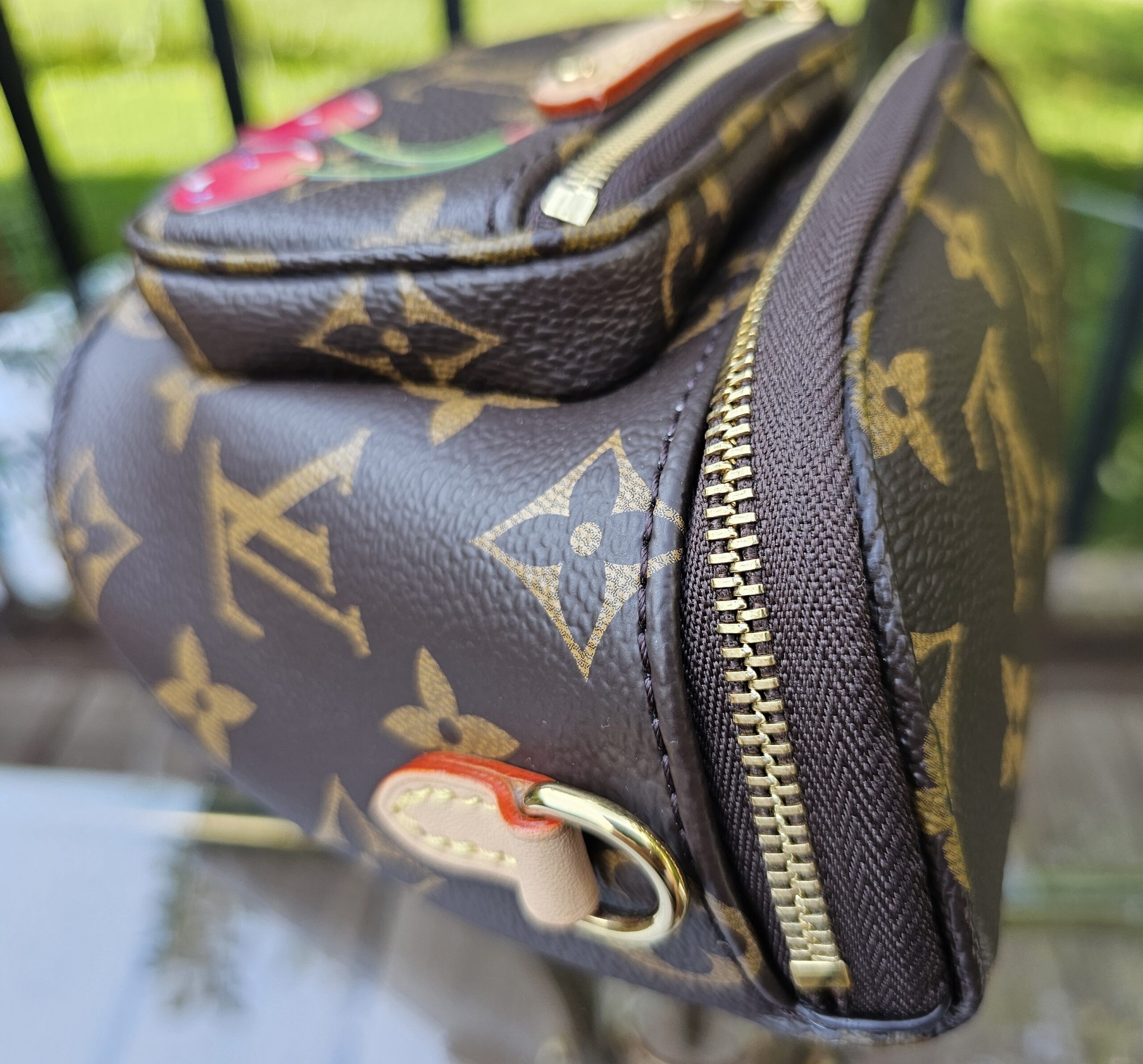 Side of the Cerises Mini Bumbag showing the curved zip and vachetta leather tab