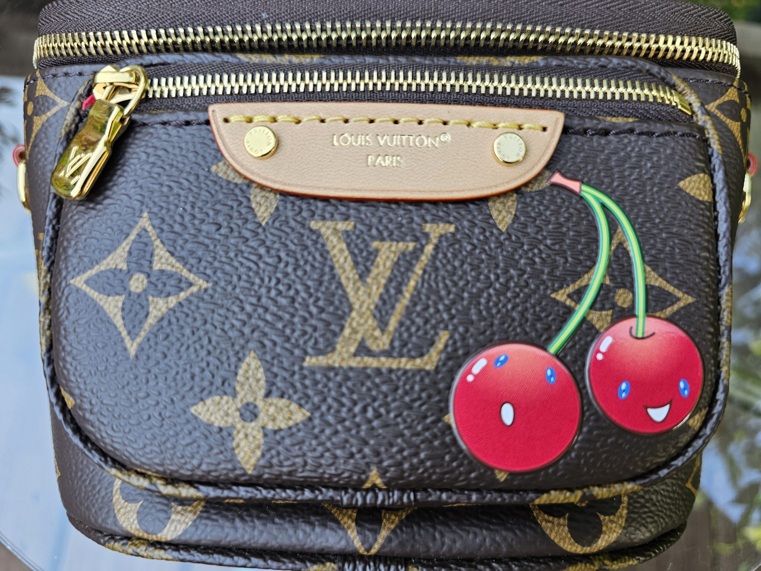 Close-up of the Takashi Murakami smiling Cerises cherry motif on the Monogram Mini Bumbag