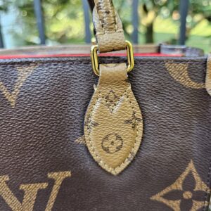 Handle tab against the giant monogram canvas of the OnTheGo PM, showing rubbing at the top edge