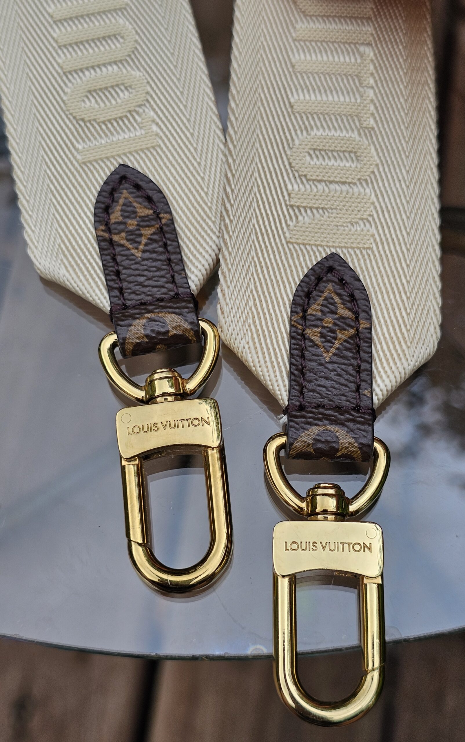 Both ends of the cream jacquard strap with Monogram tabs and snap hooks