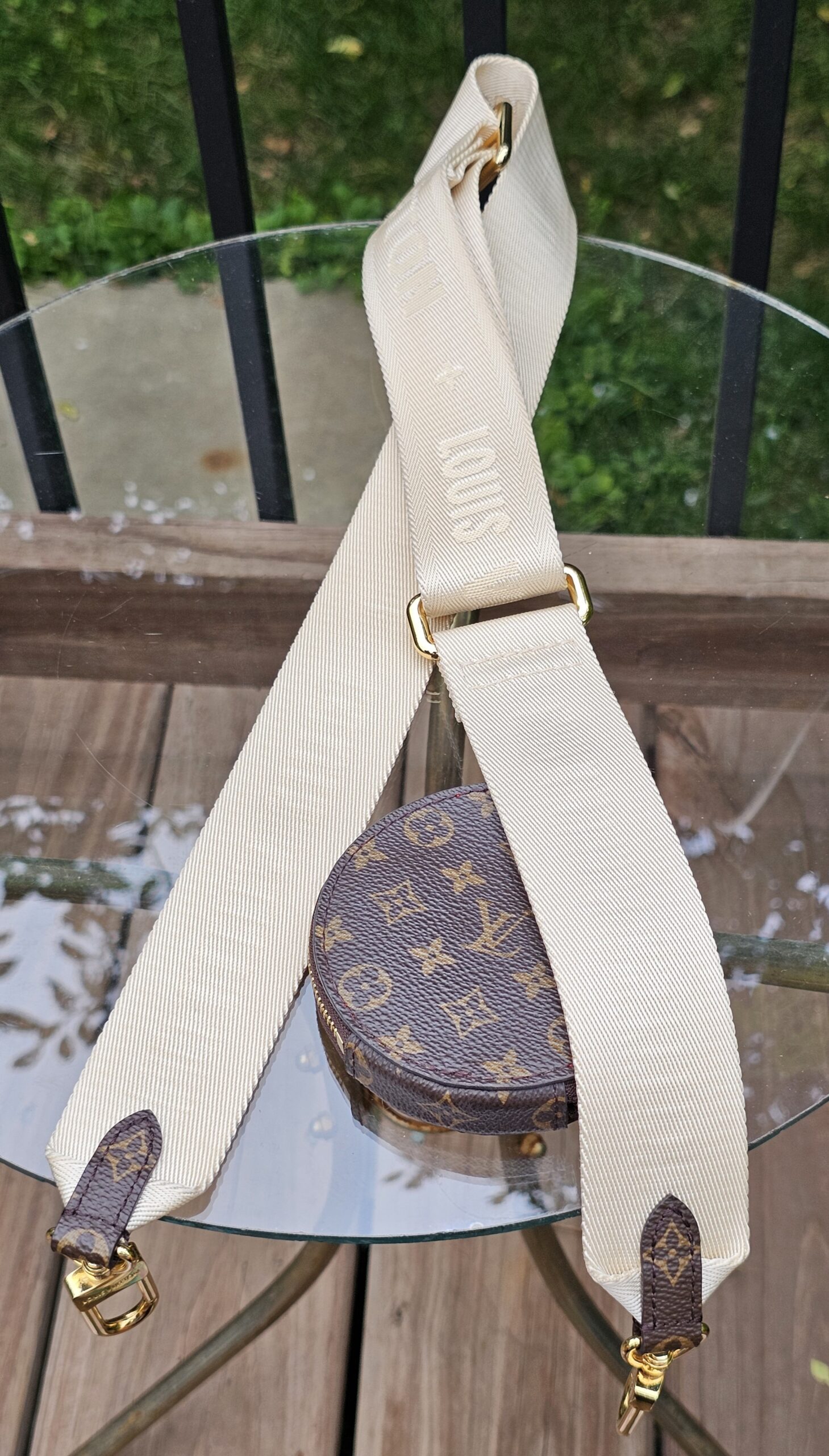 Cream jacquard adjustable strap laid out with the Monogram round pouch