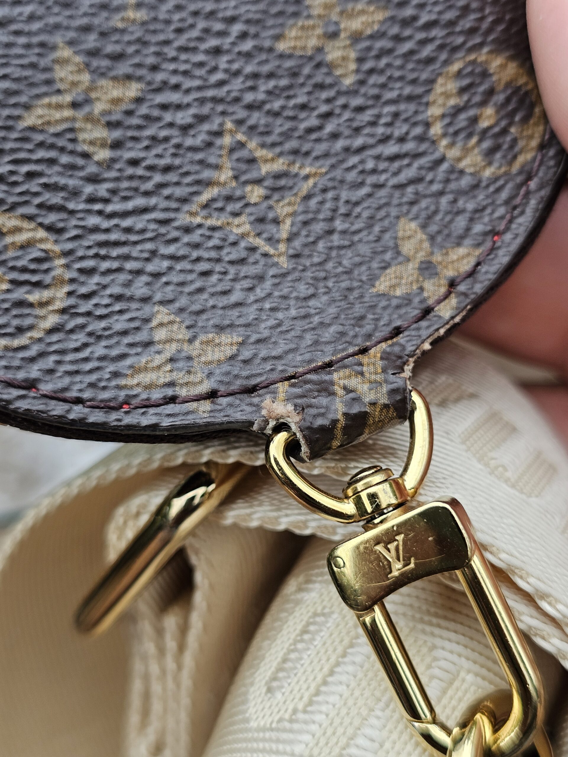 Attachment tab and snap hook on the Monogram round pouch showing edge wear